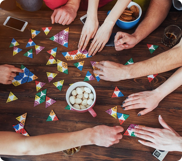 Een bovenaanzicht van mensen die aan een tafel een veelkleurige geometrische puzzel in elkaar zetten